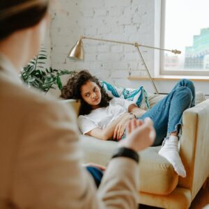 A therapist converses with a young adult on a sofa, focusing on mental health.