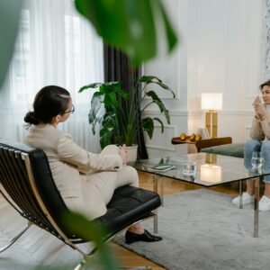 A woman in therapy, sitting across from a therapist in a modern office setting, expressing feelings.