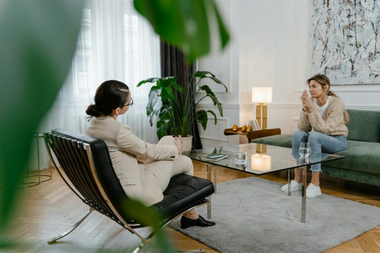 A woman in therapy, sitting across from a therapist in a modern office setting, expressing feelings.